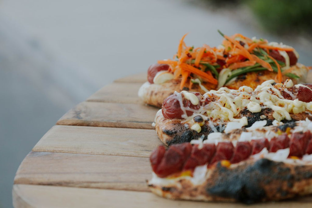 Finished trio of pizza oven hot dogs featuring classic, Thai, and Mexican street corn-inspired toppings