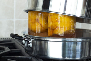 Home cook using an atmospheric steam canner to safely preserve jars of homemade jam and peaches