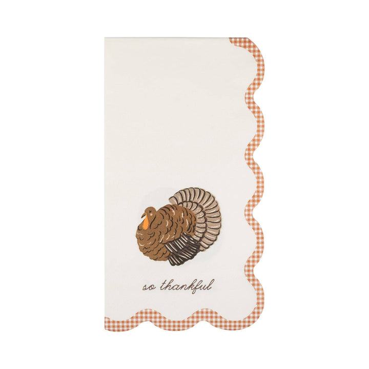 A vertical white napkin with scalloped edges, featuring a brown turkey illustration, a red-and-white gingham border, and the cursive text 'so thankful' near the bottom.