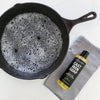 Cast iron skillet with soapy water and a bottle of cast iron soap on a white background
