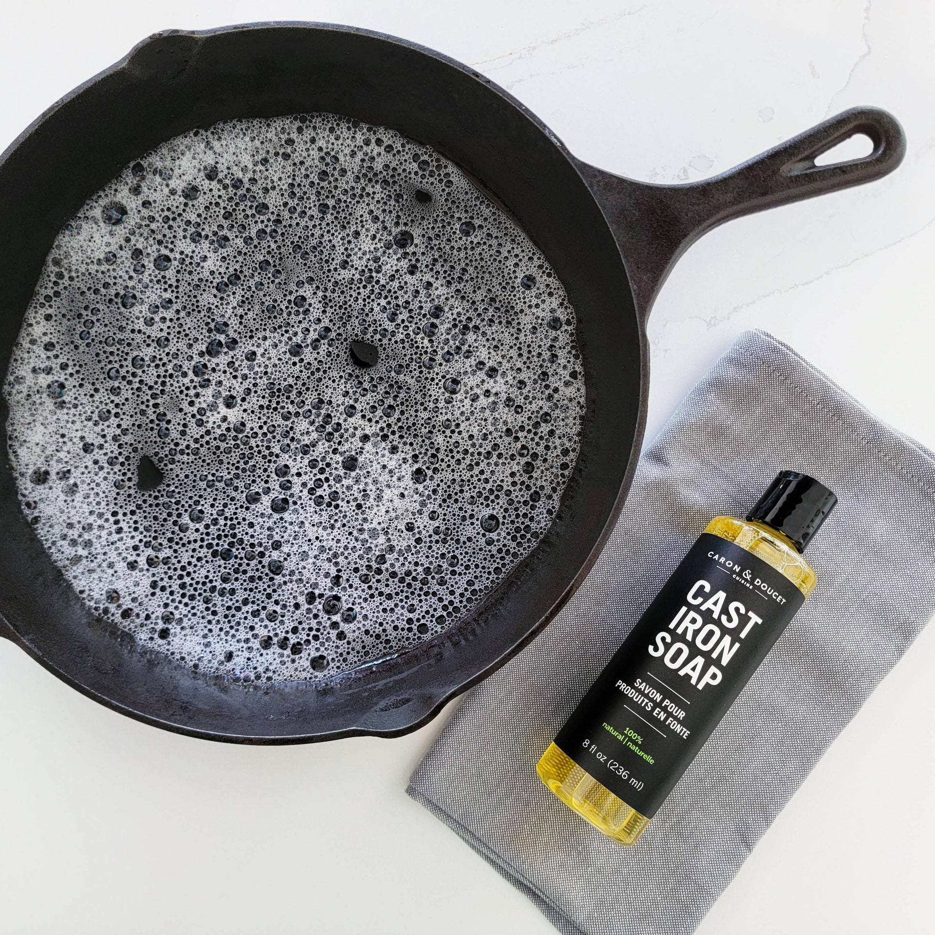Cast iron skillet with soapy water and a bottle of cast iron soap on a white background