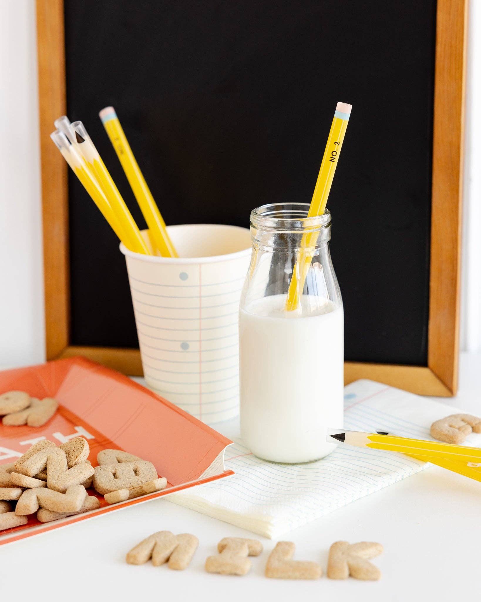 Milk bottle with a pencil-shaped straw, and alphabet cookies on a table.