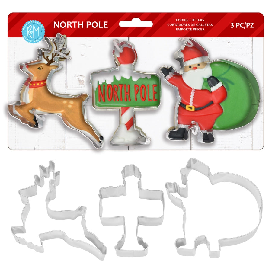 Three-piece Christmas cookie cutter set in retail packaging, featuring a reindeer, a North Pole sign, and Santa Claus, with the metal cutters displayed below the card on a white background.