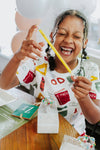 Child holding a yellow straw with a smile, wearing a colorful shirt.