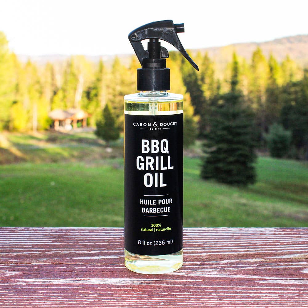 Bottle of Caron & Doucet BBQ Grill Oil on a wooden surface with a scenic background