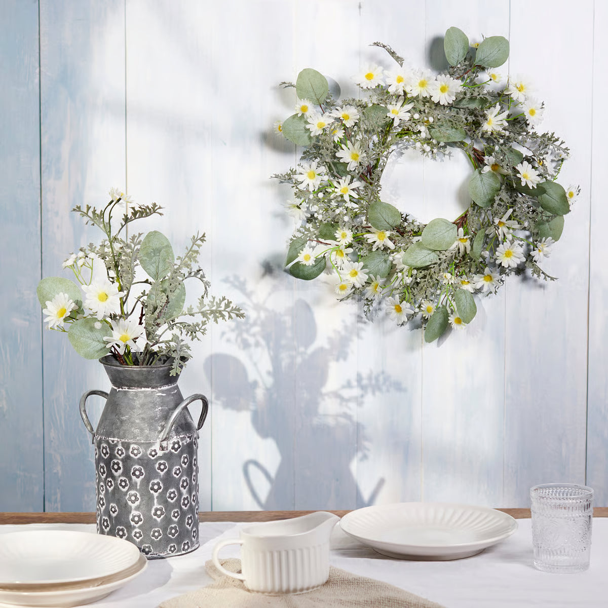 Decorative wreath and potted plant on a table with a light blue wooden background