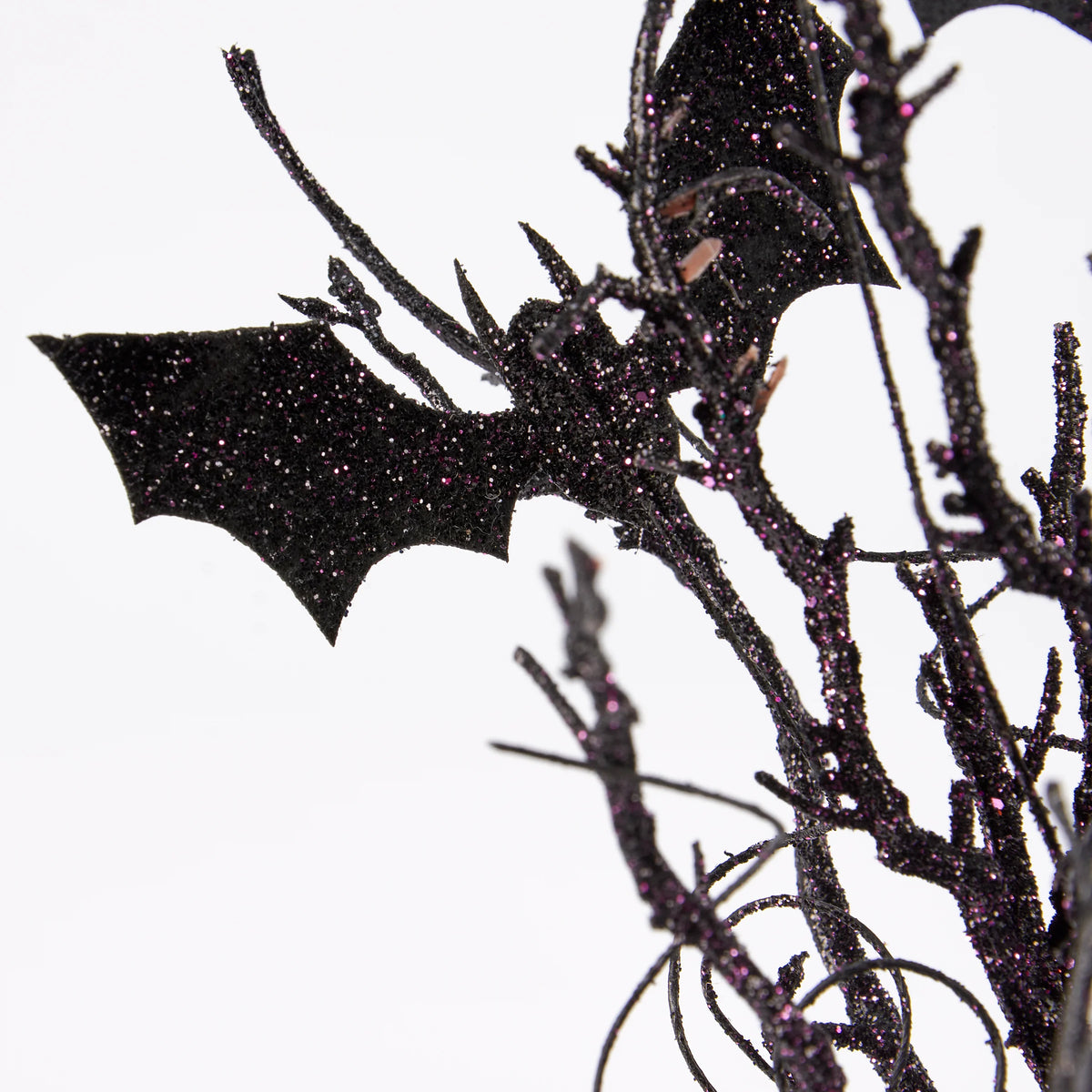Black glitter bat decoration perched on a black glitter tree branch against a plain white background.