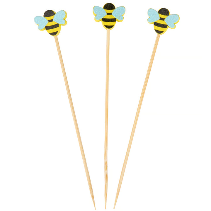Three wooden skewers with bee-shaped ends on a white background