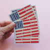 Hand holding a stack of American flag-themed playing cards against a pink background