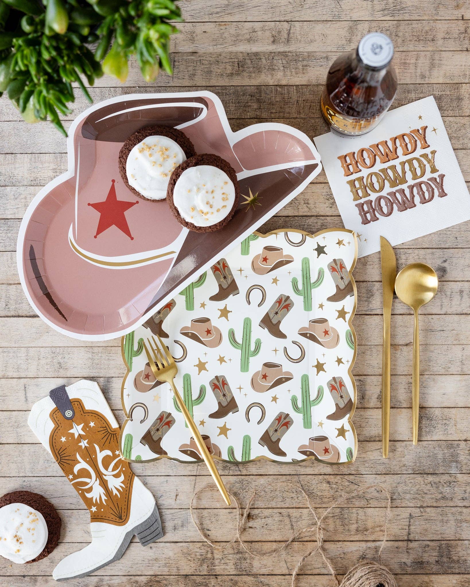 Set of cowboy-themed paper plates, napkins, and cutlery on a wooden table with a bottle of beer and plant.