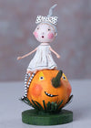 Small doll with a white dress and polka dot headband sitting on a carved pumpkin with a face.