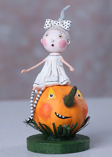 Small doll with a white dress and polka dot headband sitting on a carved pumpkin with a face.
