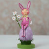 Pink bunny figurine with flowers on a decorative stand against a blurred background