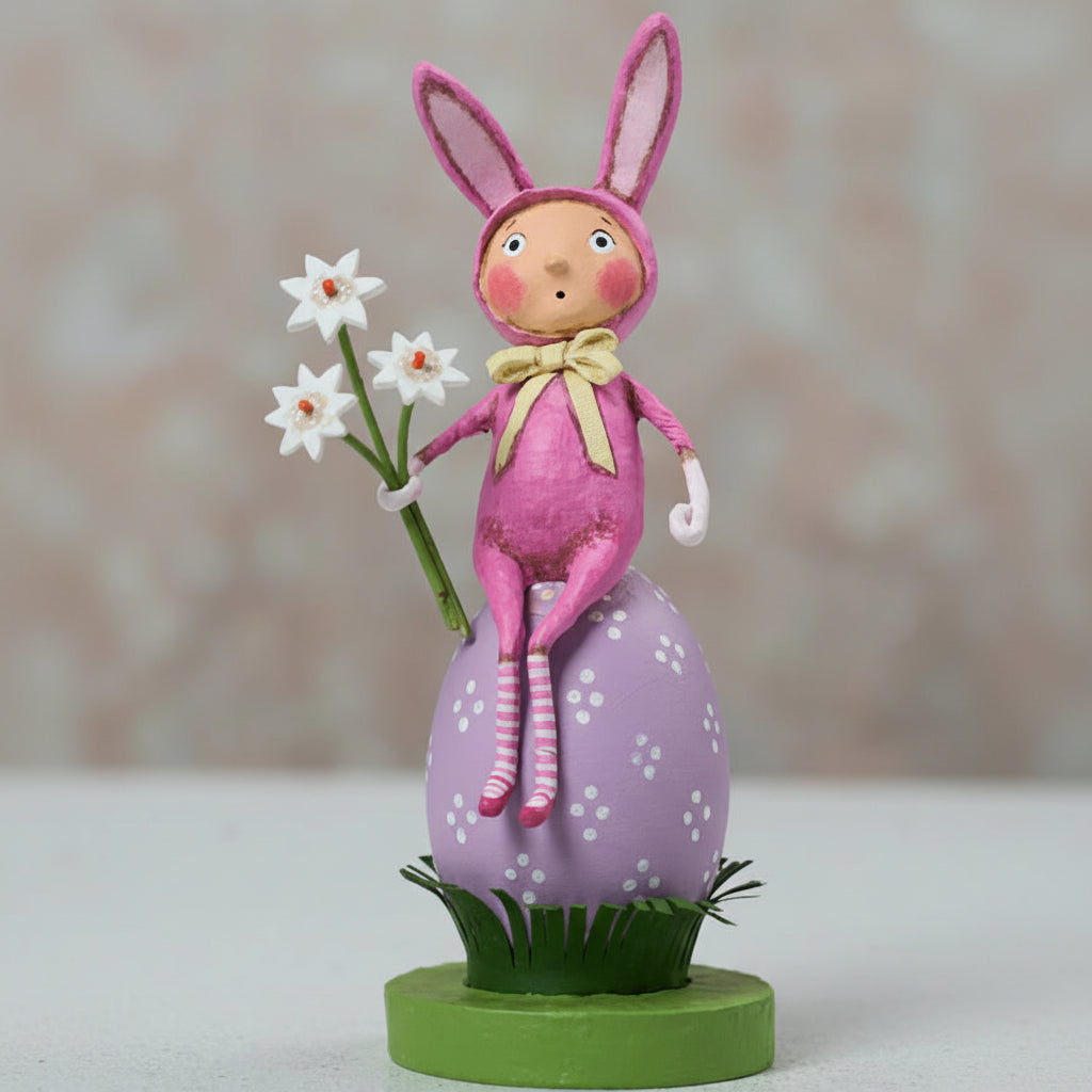 Pink bunny figurine with flowers on a decorative stand against a blurred background