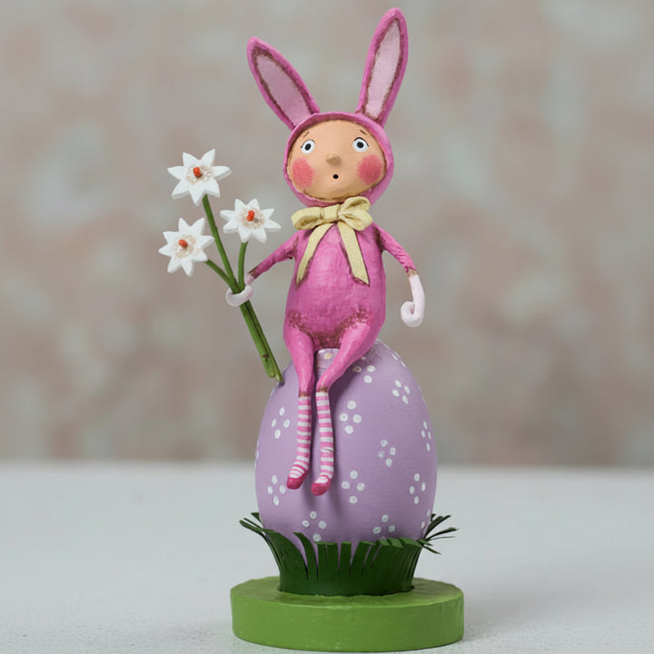 Pink bunny figurine with flowers on a decorative stand against a blurred background