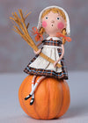 Decorative figurine of a girl in pilgrim attire sitting on a pumpkin with a stalk of wheat, against a neutral background.