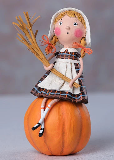 Decorative figurine of a girl in pilgrim attire sitting on a pumpkin with a stalk of wheat, against a neutral background.