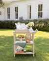 Decorative cart with Easter-themed items on a grassy lawn in front of a white house.