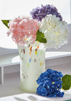Decorative vase holding pink, white, purple , and blue flowers on a white surface.
