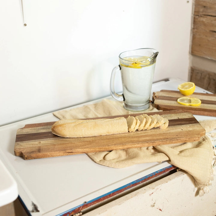 Wooden cutting board with bread and a pitcher of lemon water on a kitchen counter.