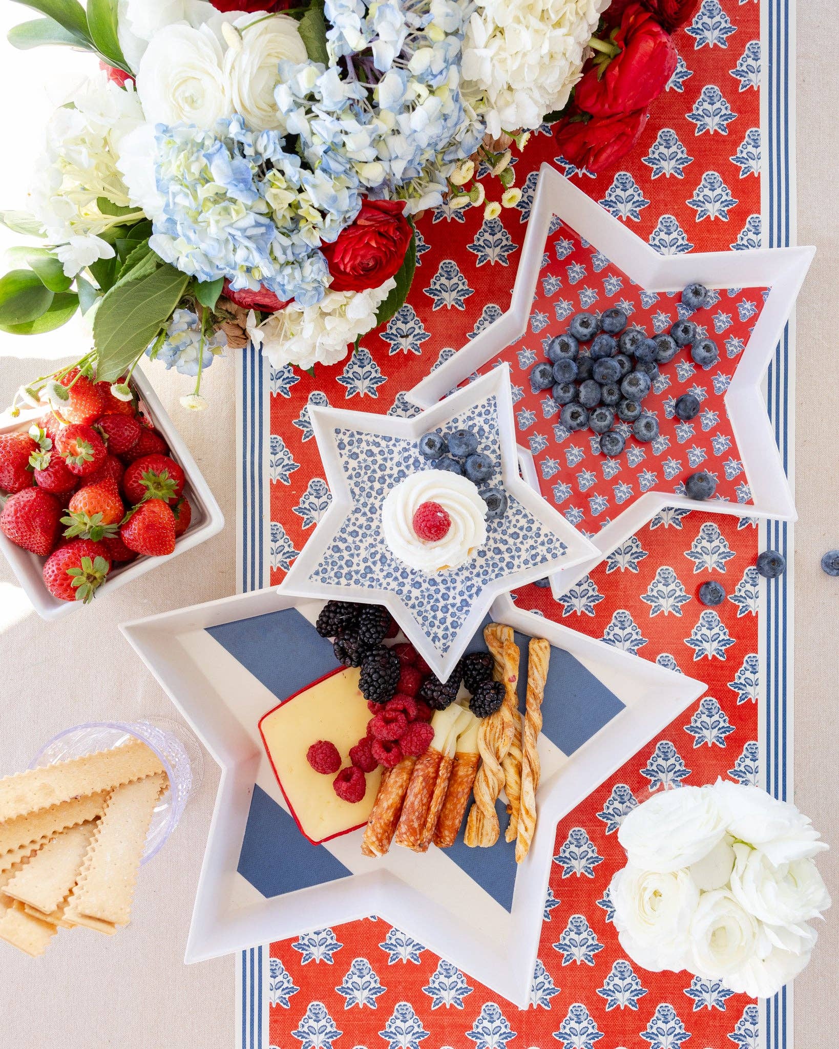 Star-shaped trays with snacks on a decorative tablecloth with flowers and berries.