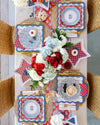Decorative table setting with red, white, and blue plates, trays and flowers.