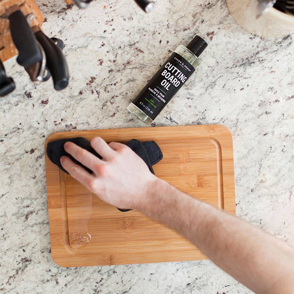 Person applying cutting board oil to a wooden cutting board on a granite countertop.