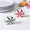 Peppermint candy-shaped salt and pepper shakers on a kitchen counter with plates and a towel in the background.