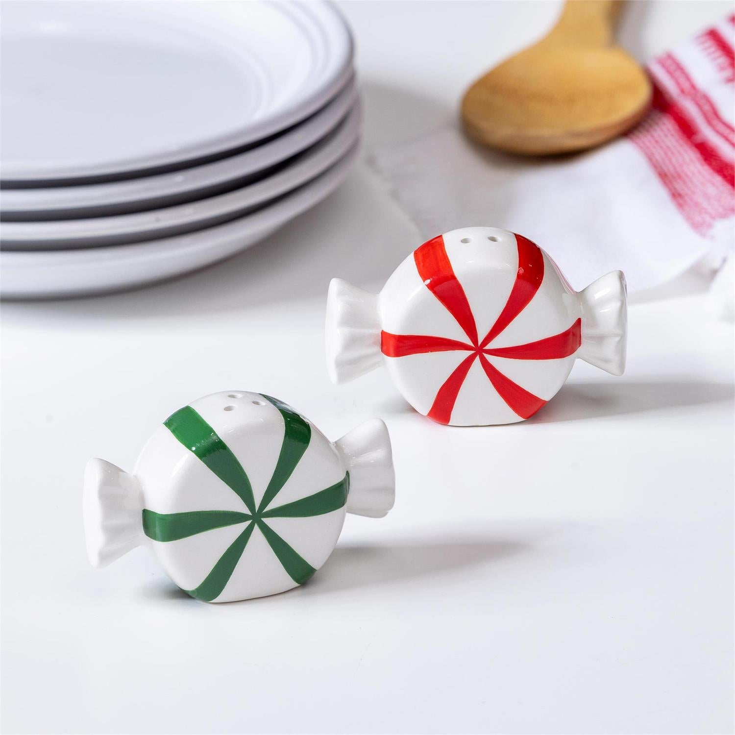 Peppermint candy-shaped salt and pepper shakers on a kitchen counter with plates and a towel in the background.