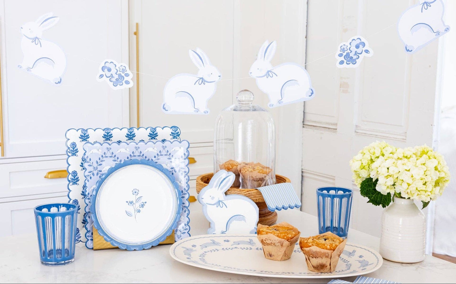 Decorative Easter setting with bunny figurines, plates, and pastries on a white surface.