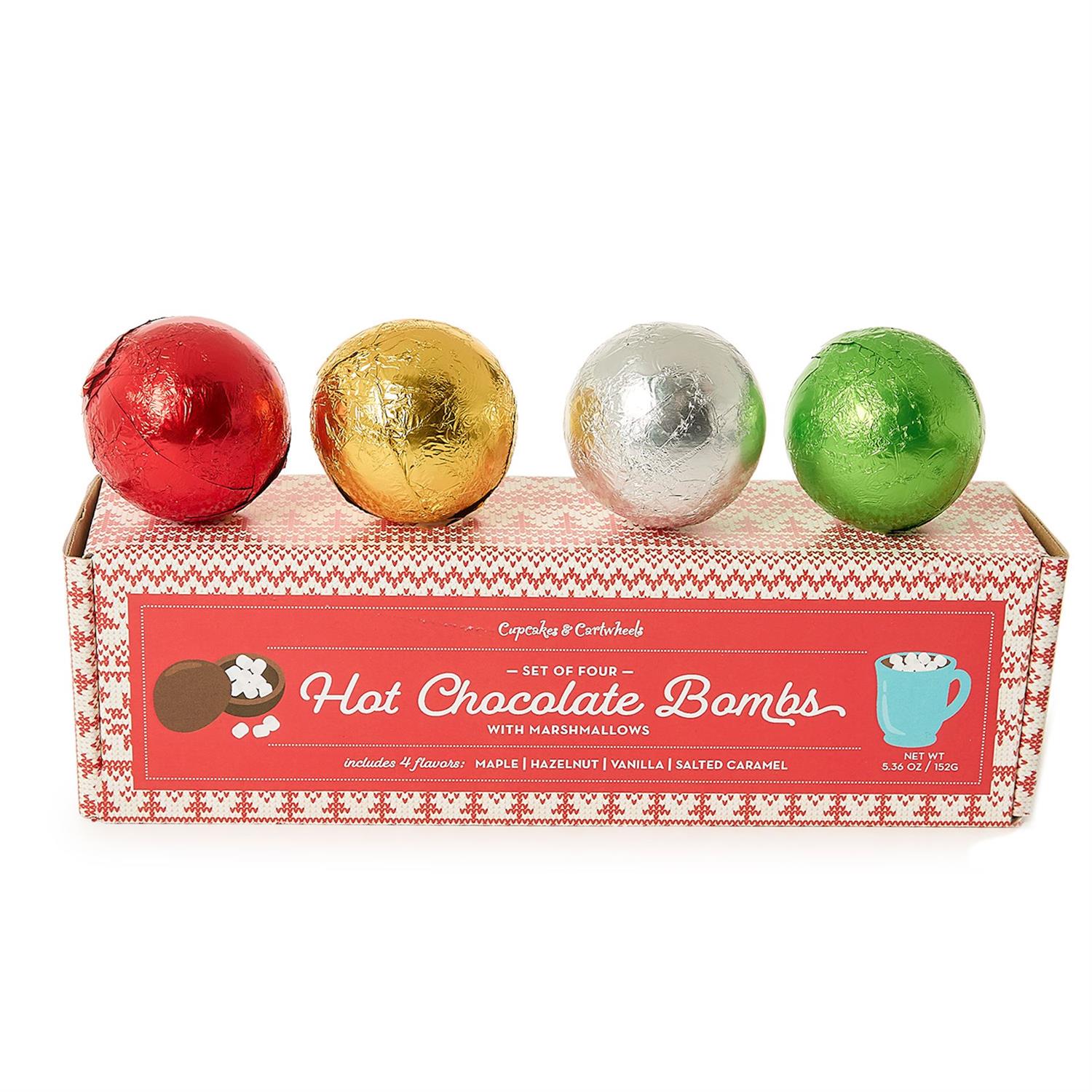 Four hot chocolate bombs in red, gold, silver, and green foil packaging on a white background.