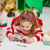 Child playing with a toy train set on a white surface with a Christmas-themed sweater and headband.