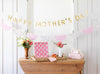 Decorative setup with 'Happy Mother's Day' banner, flowers, and gift on a wooden table.