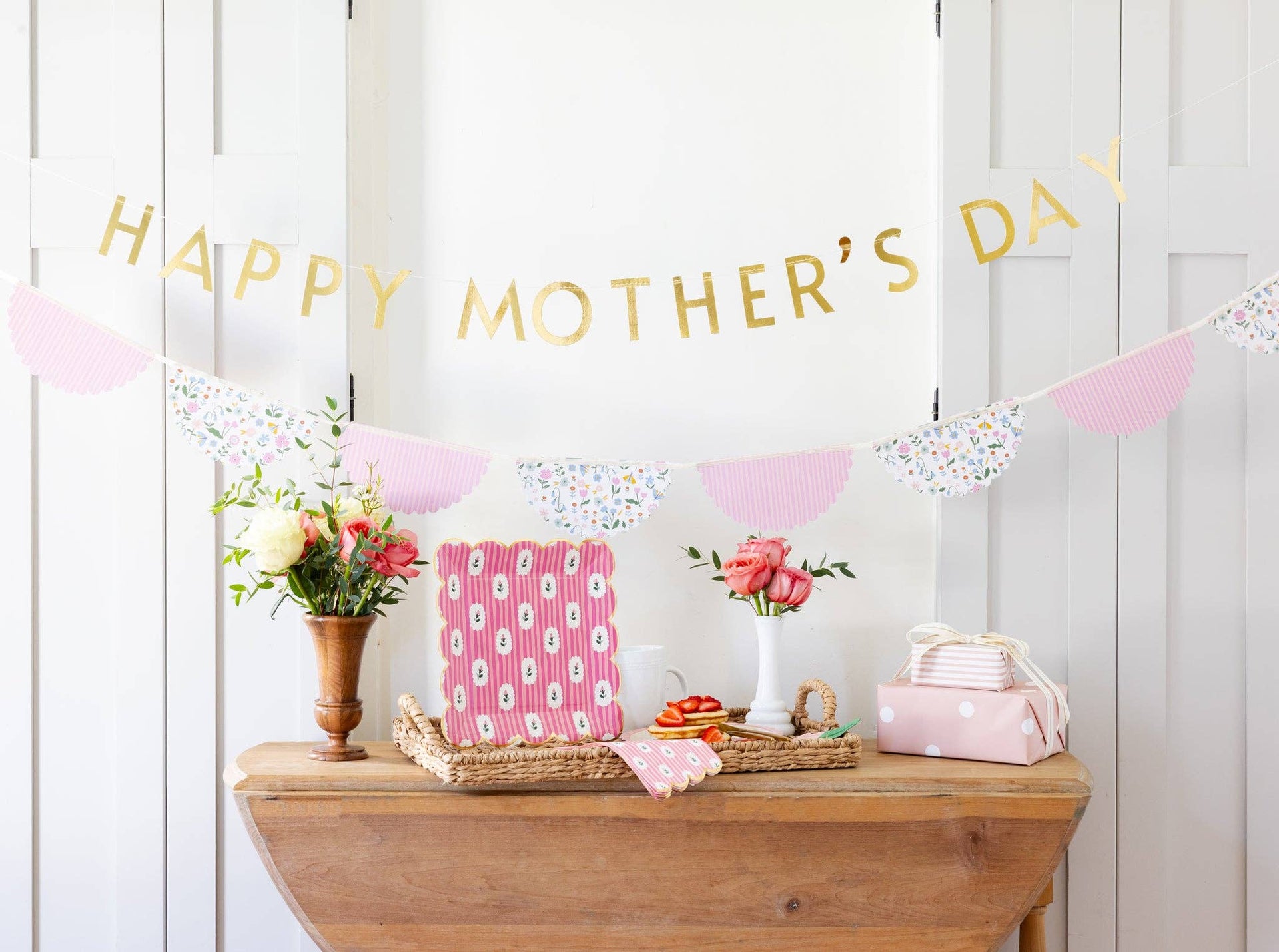 Decorative setup with 'Happy Mother's Day' banner, flowers, and gift on a wooden table.