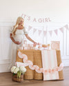 Woman standing next to a baby shower table with 'It's a Girl' banner.