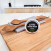 Cutting board wax container on a wooden cutting board with wooden utensils in a kitchen setting