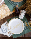 Set of paper plates, napkins, and a bottle on a rustic wooden table with a bandana and hay in the background.