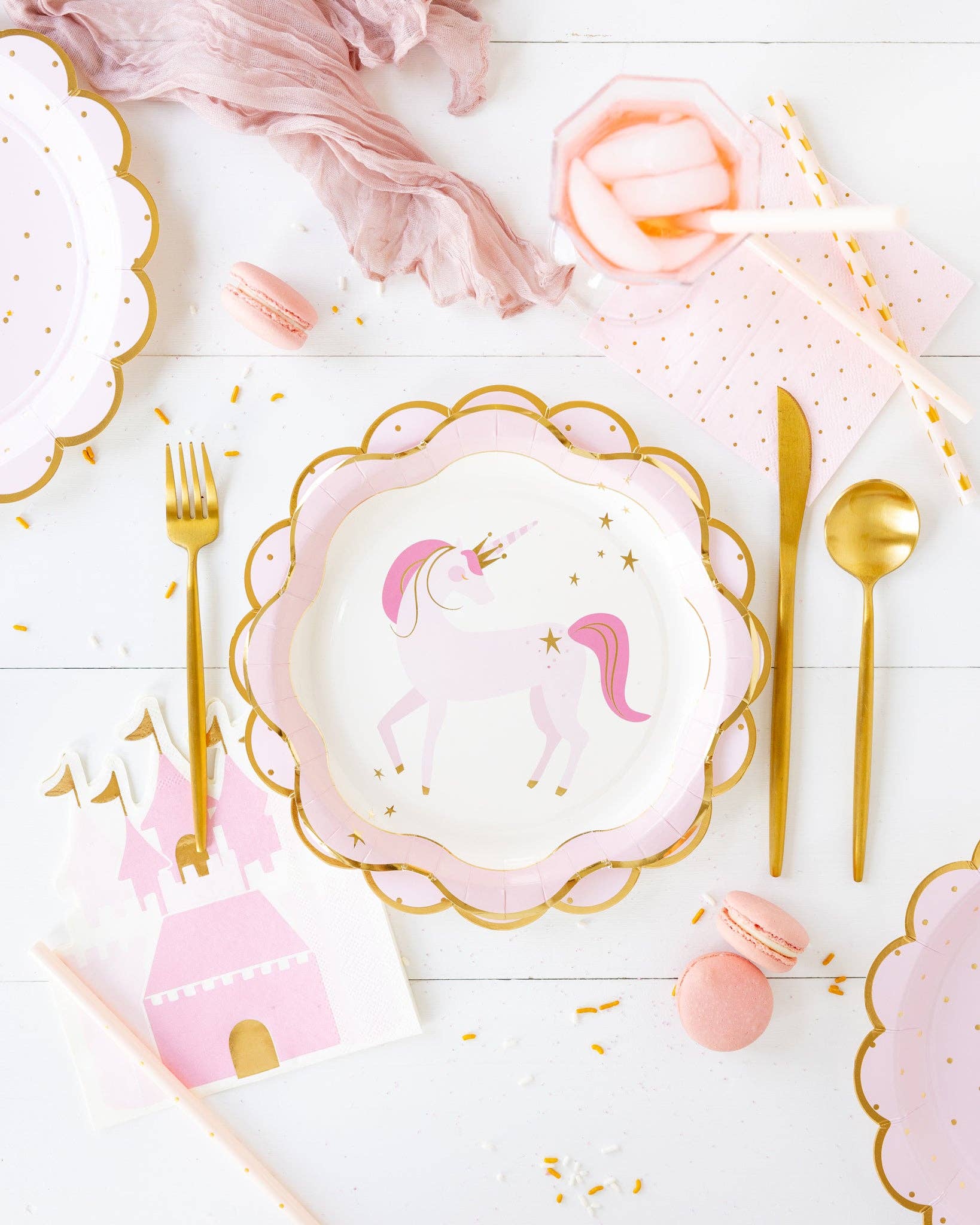 Table setting with unicorn-themed plates, pink castle napkins, and gold cutlery on a white surface.