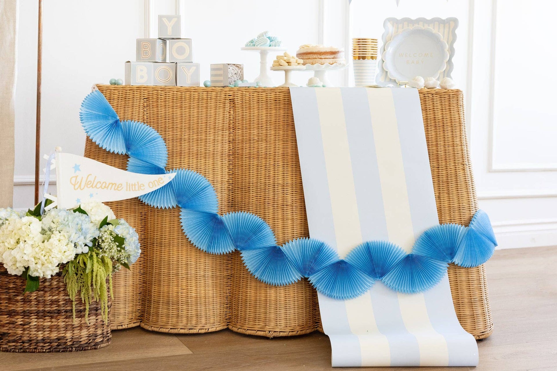 Decorative blue paper garland and blue and white striped table runner on a white and brown table with flowers and decor items.