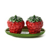 Two strawberry-shaped ceramic salt and pepper shakers on a green plate with a white background.