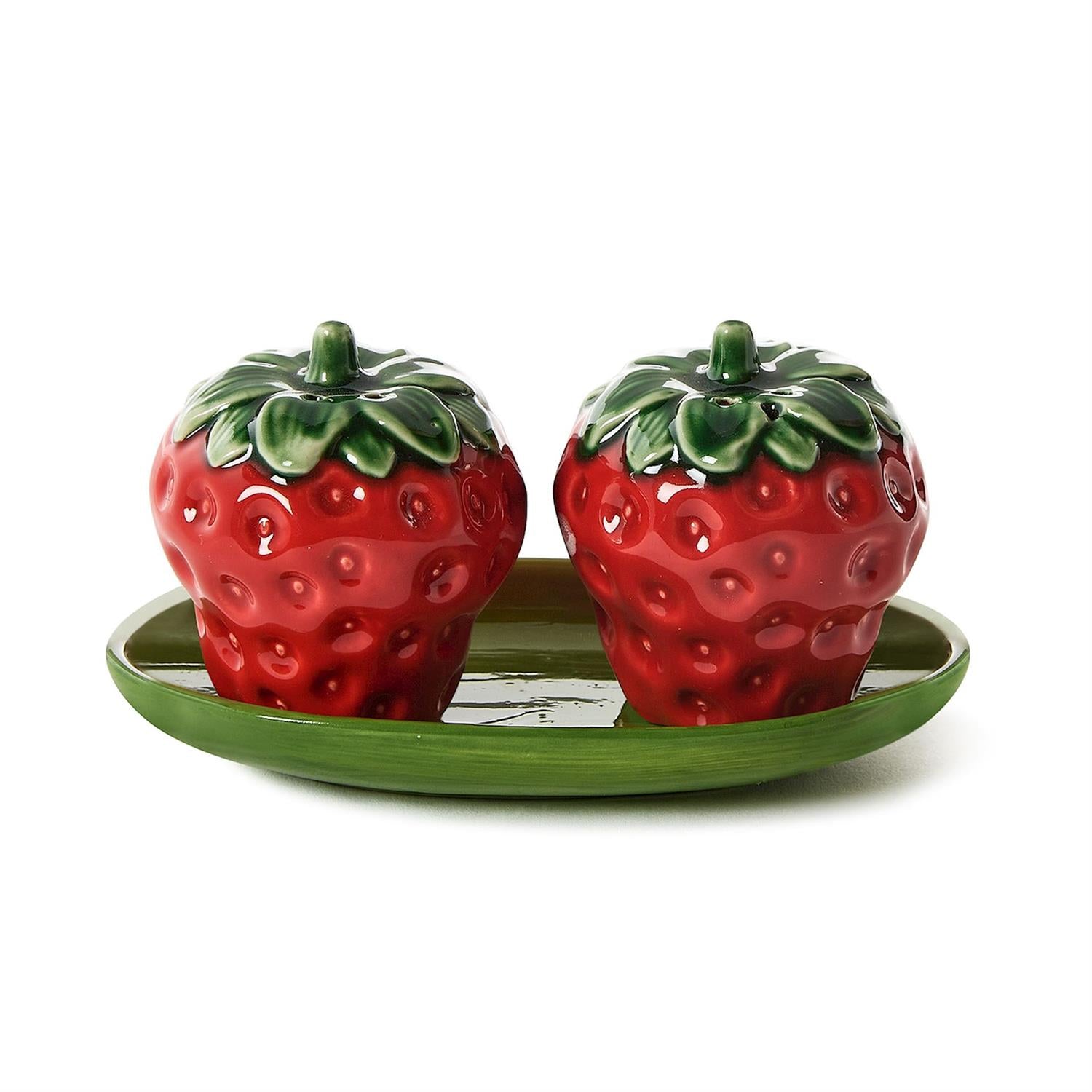 Two strawberry-shaped ceramic salt and pepper shakers on a green plate with a white background.