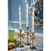 Three gold candle holders with bow design holding white candles on a table with a blue wall and decorative elements in the background.
