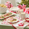 Christmas-themed table setting with hot chocolate, cookies, and poinsettias, featuring white scalloped-edge serving dishes.