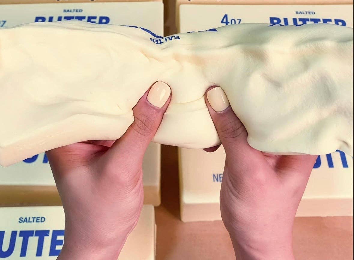 Hands holding a butter squishy toy with butter boxes in the background
