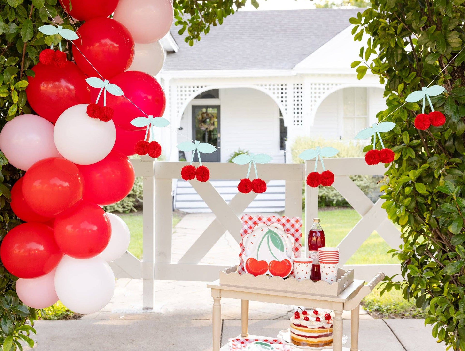 Decorative setup with balloons, cherry-themed decor, and a cake on a table outdoors.