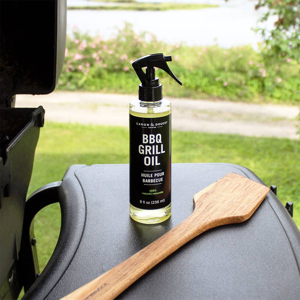 Bottle of BBQ grill oil on a grill with a wooden spatula, outdoor setting.