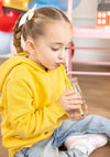 Child in a yellow hoodie drinking from a milk carton with a pencil-shaped straw in an indoor setting.