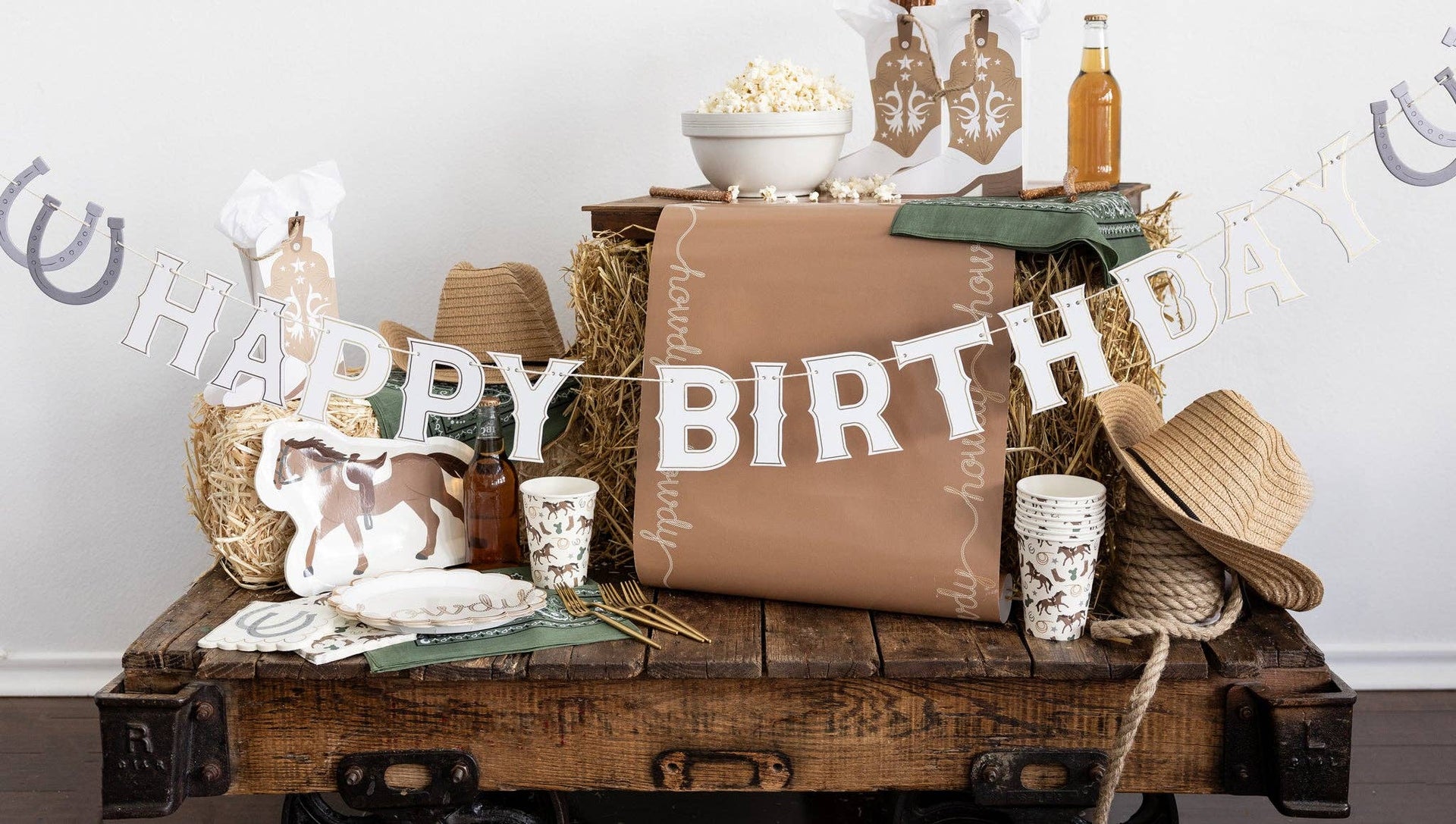 Decorative birthday setup with 'Happy Birthday' banner, hats, and drinks on a wooden table.