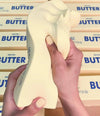 Hand holding a butter squishy toy with stacked butter packages in the background