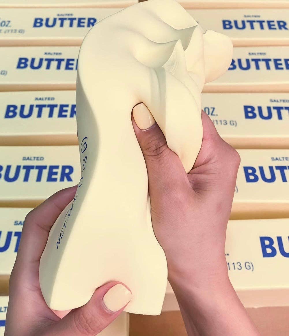 Hand holding a butter squishy toy with stacked butter packages in the background